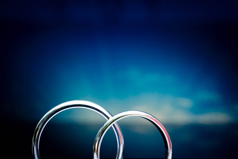 Hochzeitsringe des Brautpaares als Detailfoto vor blauen Hintergrund